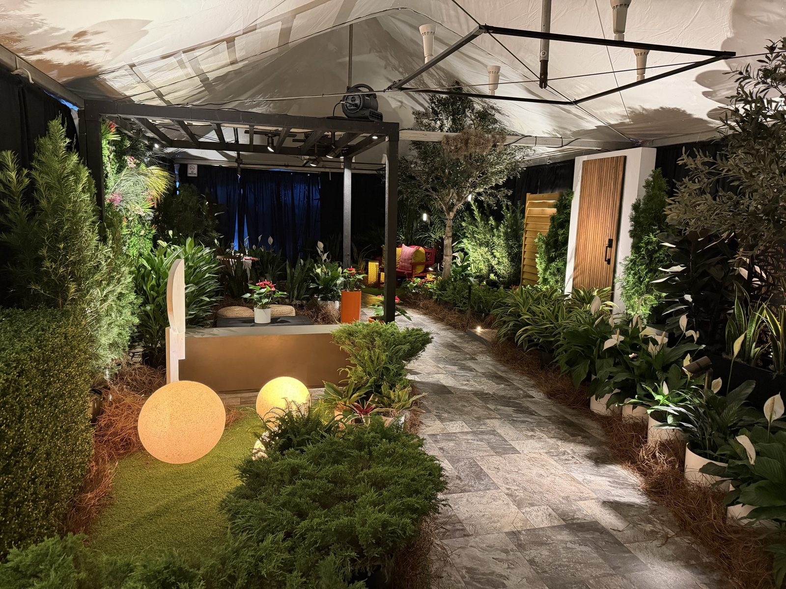 Landscaped outdoor lighting vignette at CEDIA Expo 2026 with illuminated orb path lights, a stone walkway, and layered planting under a pergola