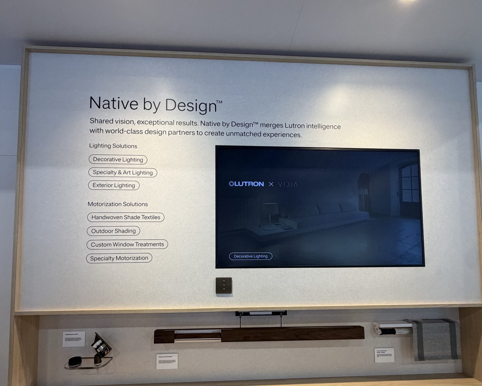 Lutron Native by Design booth board at CEDIA Expo 2026 listing exterior lighting and outdoor shading, with a Coastal Source VIA fixture and Palladiom drapery track displayed below