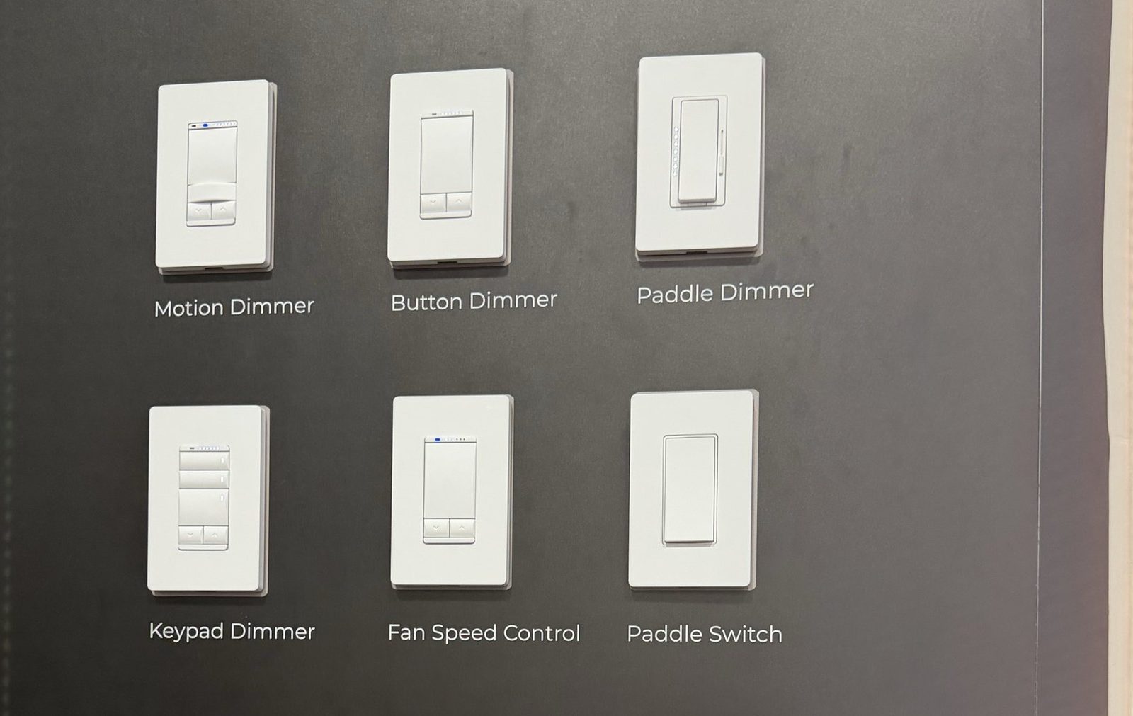 GE Proseo Flex white keypads and dimmers on a dark wall at CEDIA Expo 2026, including motion, button, and paddle dimmers and a fan speed control