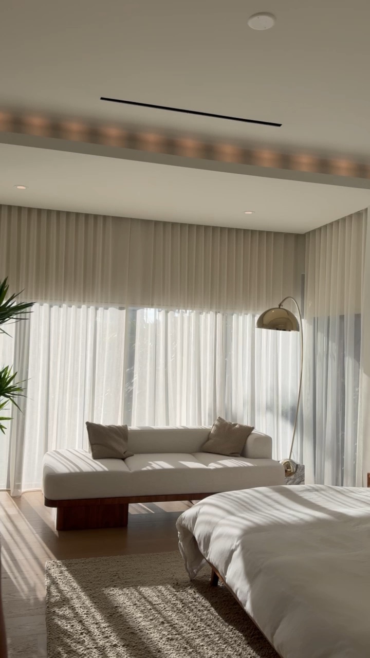 Late-afternoon sun casting warm rays through sheer drapery onto a daybed, with a warm cove glow along the ceiling
