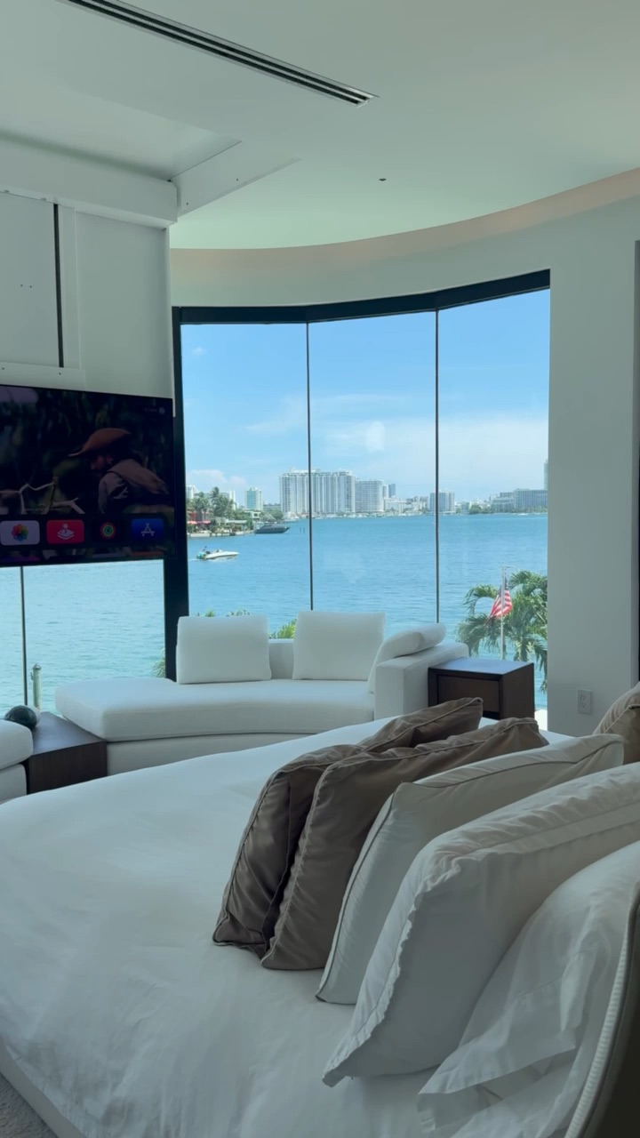 Curved floor-to-ceiling glass wall facing Biscayne Bay in a waterfront primary bedroom