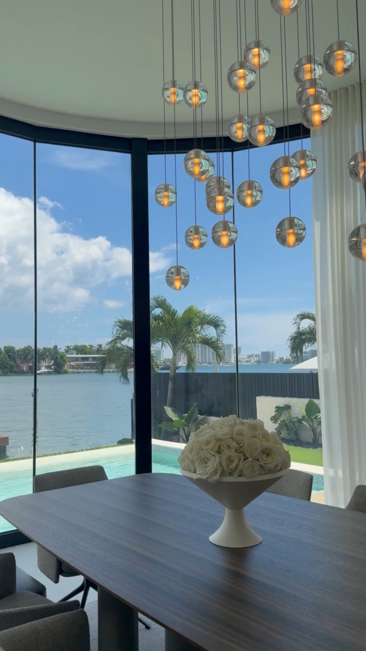 Warm glass-orb pendants glowing against a bright bay view through curved floor-to-ceiling glass
