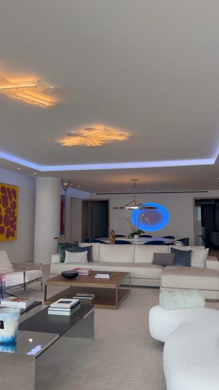 Living room with warm sculptural ceiling fixtures, saturated blue cove lighting and a backlit art niche
