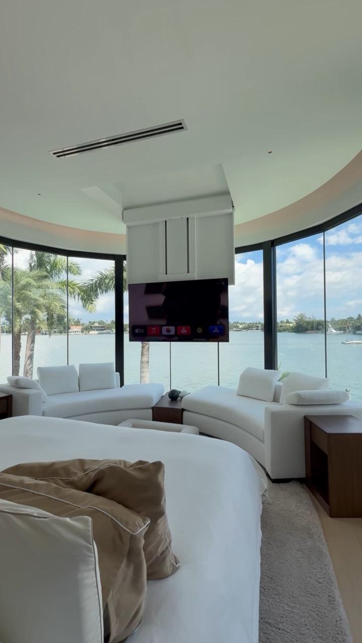 Motorized ceiling TV lift lowering a display from a recessed ceiling pocket in a curved-glass waterfront bedroom