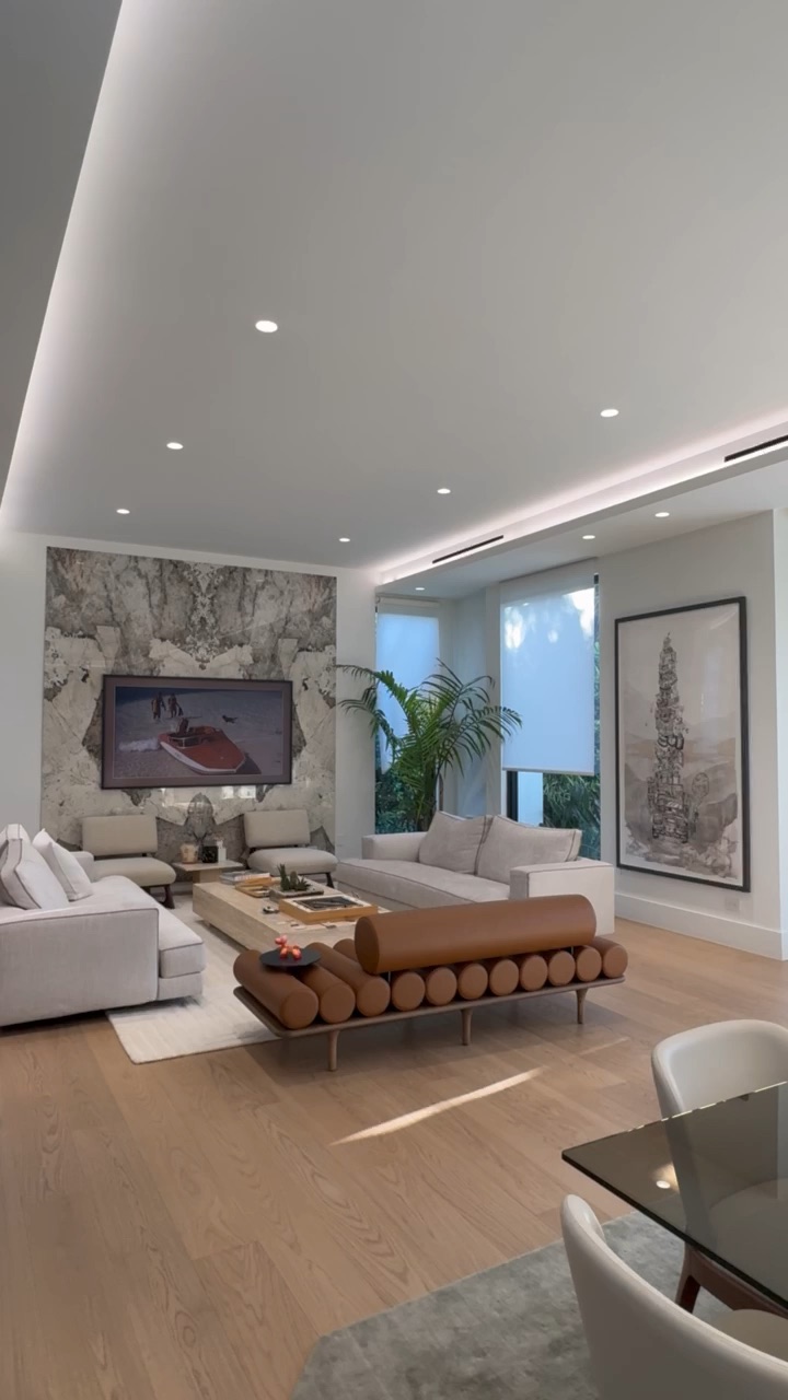 Living room with continuous cove lighting, recessed downlights, a frame TV set into a stone feature wall, and motorized roller shades