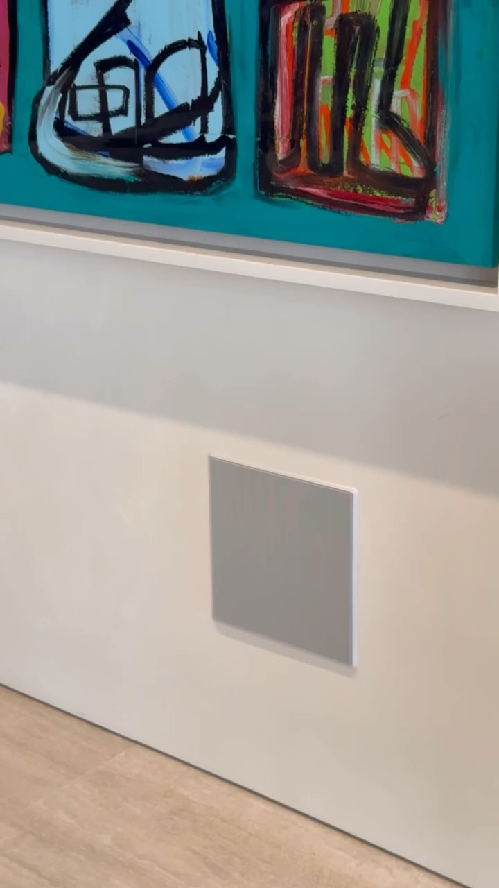Flush plaster-in wall speaker set into a white millwork panel beneath a large abstract painting