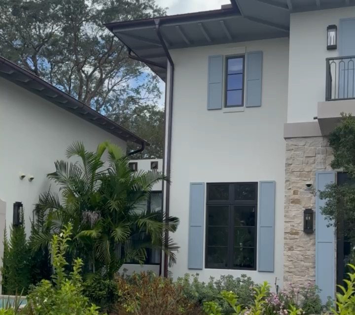 South Florida home exterior with security cameras mounted under the eaves, stone accent facade, and tropical landscaping