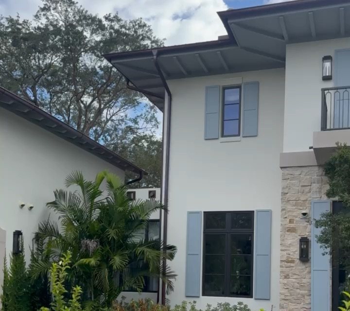 South Florida luxury home exterior with security cameras, stone facade, blue shutters, and tropical landscaping