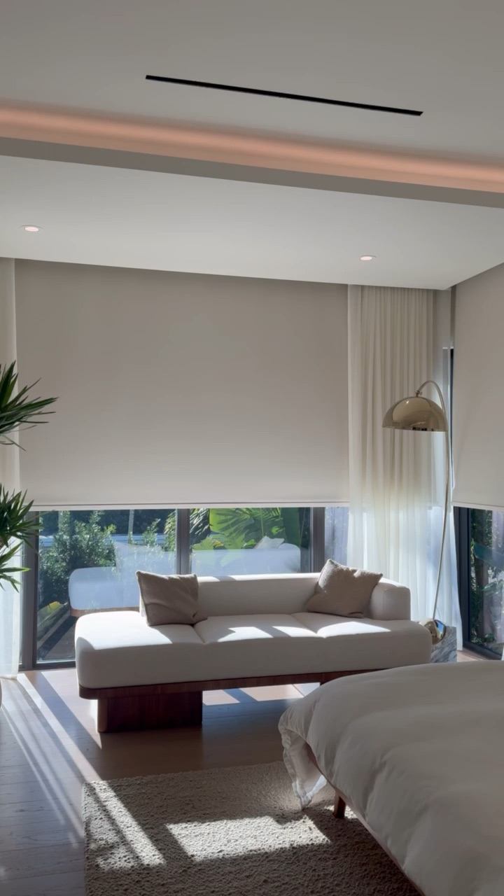 Motorized roller shade half-lowered behind sheer drapery
