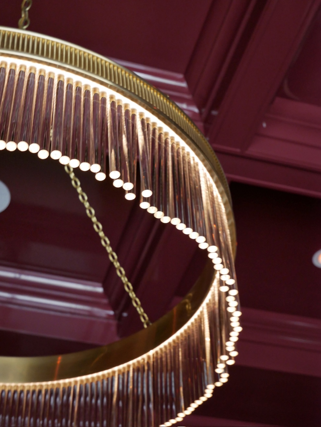 Close view of a champagne glass-rod chandelier glowing against a dark lacquered coffered ceiling