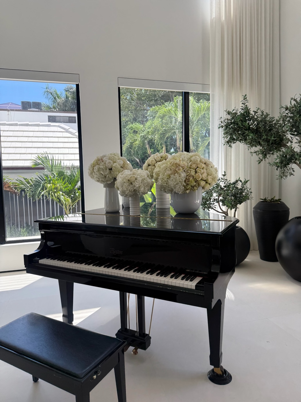 Black grand piano with white floral arrangements in a bright living room with palm views
