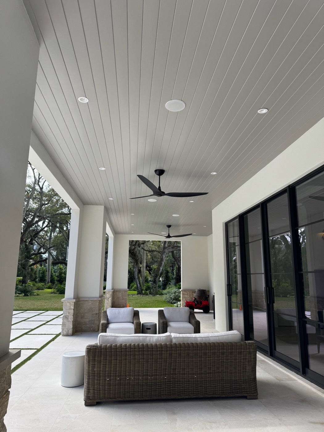 Covered lanai with flush in-ceiling speakers and black ceiling fans above wicker seating